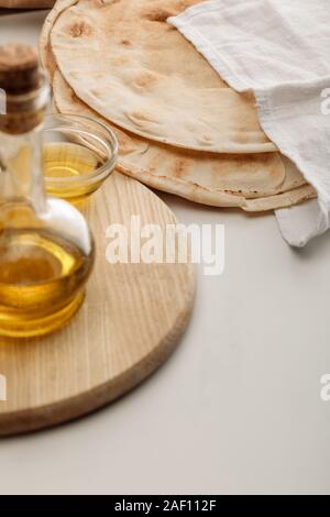 Pain lavash couverts avec serviette près de planche à découper avec de l'huile sur la surface blanche Banque D'Images