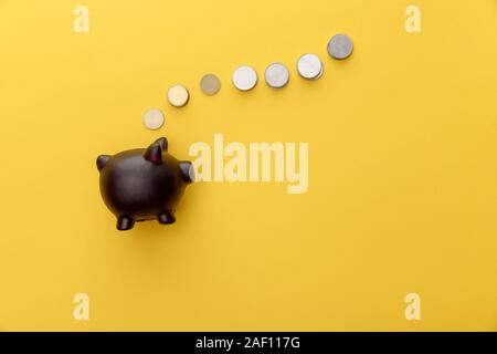 Vue de dessus de tirelire noir sur fond jaune avec des pièces de monnaie Banque D'Images