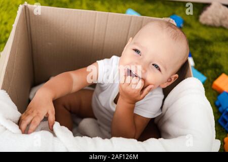 Cute blue-eyed child sitting and smiling in cardboard box with blanket Banque D'Images