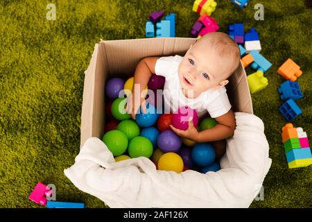 Vue de dessus de l'enfant mignon en boîte carton jouant avec boules colorées Banque D'Images