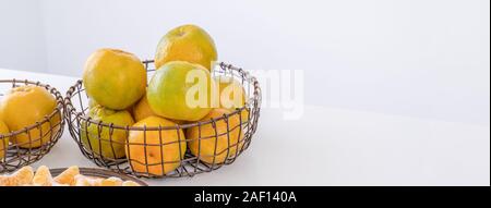Belles mandarines pelées dans une assiette et panier métal isolé sur blanc brillant table propre dans une cuisine contemporaine et moderne, l'île close up. Banque D'Images