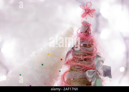 Petits arbres de Noël décoratifs faits main mignons en dentelle blanche, ficelle organique et noeuds sur fond de bokeh de lumières blanches. Banque D'Images