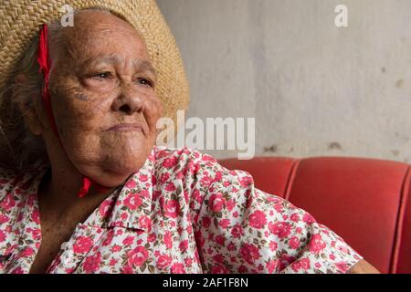 Penedo, Alagoas, Brésil - 04 juillet 2016 : femme brésilienne traditionnelle avec un chapeau de paille, assise sur un canapé rouge à la maison Banque D'Images