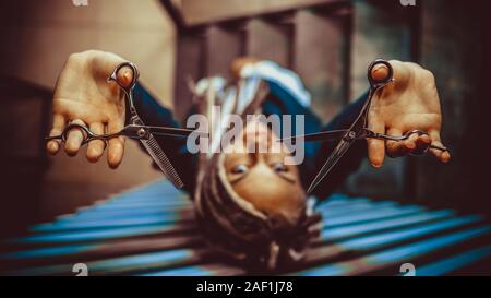 Coiffure femme avec des dreadlocks holding scissors in hand close-up Banque D'Images