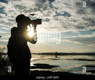 Photographe photo prise mâle, debout à l'extérieur avec soleil levant glowing derrière lui. Banque D'Images