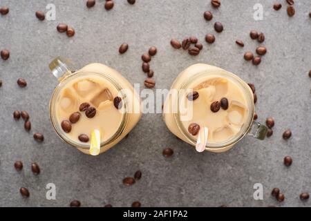 Vue de dessus de café de glace dans des bocaux en verre avec des pailles et grains de café sur fond gris Banque D'Images