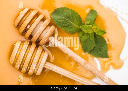 Vue rapprochée de balanciers en bois dans le miel miel flaque de feuilles de menthe isolated on white Banque D'Images