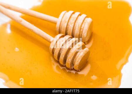 Vue rapprochée de balanciers en bois dans le miel miel flaque isolated on white Banque D'Images
