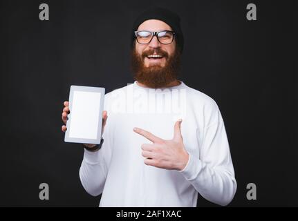 Portrait de jeune homme barbu pointant à l'écran vide sur tablet Banque D'Images