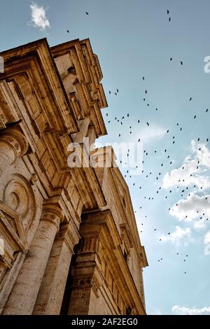 Un grand troupeau / meurtre de corbeaux volant au-dessus de la fin de l'architecture Renaissance façade d'église de San Biagio, Montepulciano, Toscane, Italie EU Banque D'Images