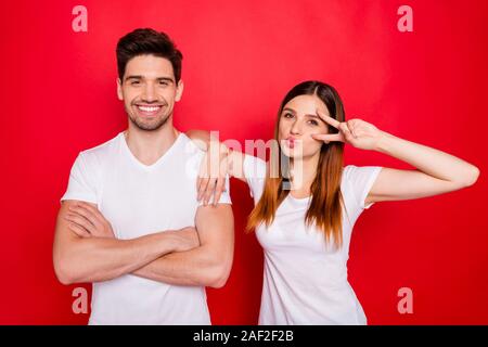 Photo de nice positive joyeux couple charmant petit ami petite amie de port blanc T-shirt montrant v-signe avec les mains pliées smiling toothily Banque D'Images