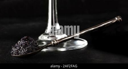 Black caviar sur une cuillère, un verre de champagne, un gros plan sur un fond noir Banque D'Images