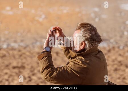 Un homme à l'aide de son smartphone pour photographier un coucher de soleil. Banque D'Images