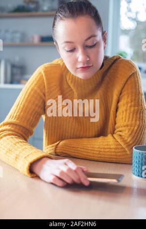 Femme inquiète de l'utilisation excessive des médias sociaux portant sur téléphone mobile sur la table Banque D'Images