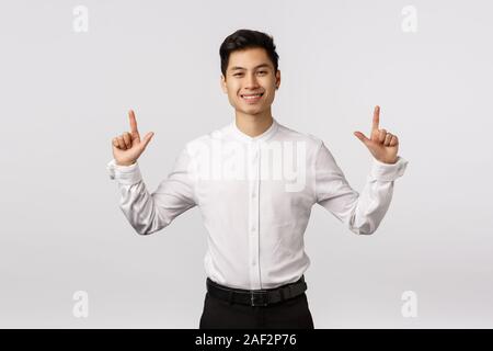Hansdome asian businessman en chemise blanche, pantalon noir, pointer du doigt et souriant de plaisir, satisfait ou heureux expression, produit Banque D'Images