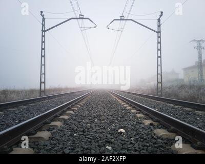 Les voies ferrées et de poteaux caténaires disparaître dans un épais brouillard. Concept de train Banque D'Images