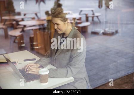 Smiling young woman working on laptop in cafe Banque D'Images