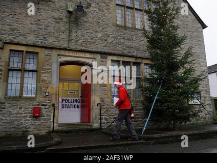 Yorkshire Dales postman Andrew Pilkington wearing a santa hat qu'il livre le courrier dans Aysgarth, Yorkshire du Nord, en passant devant le bureau de scrutin dans le Village Hall de l'Institut qui est l'affichage d'un grand arbre de Noël. Banque D'Images