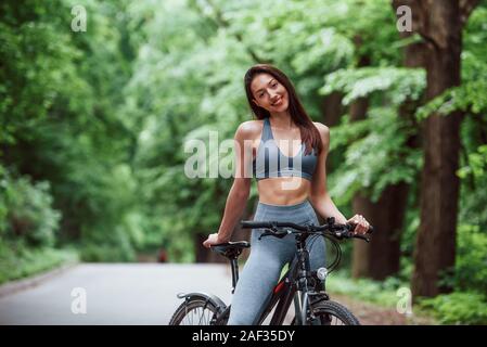 Beaucoup de week-end en bonne santé. Cycliste Femme debout avec vélo sur route asphaltée dans la forêt dans la journée Banque D'Images