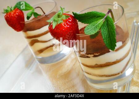 Recette de cuisine italienne Tiramisù. Dessert typiquement italien servi dans des verres avec des couches de fromage mascarpone, biscuits, café et de fraises à la menthe Banque D'Images