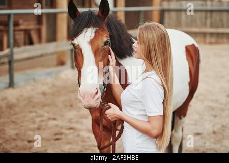 Elle aime ce qu'elle fait sur son travail. Femme heureuse avec son cheval dans le ranch de la journée. Banque D'Images