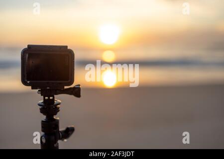 GoPro Hero 7 sur un trépied sur une plage à Rio pour le rubanage et regarder le lever du soleil avec le soleil se reflétant dans l'eau de mer Banque D'Images