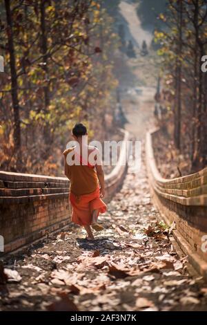 Un jeune moine bouddhiste escalade l'escalier menant au temple Wat Phra Non à Mae Hong Son, Thaïlande. Banque D'Images