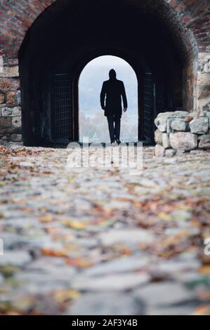 Silhouette d'un jeune homme marchant à travers un tunnel comme entrée d'une vieille forteresse Banque D'Images