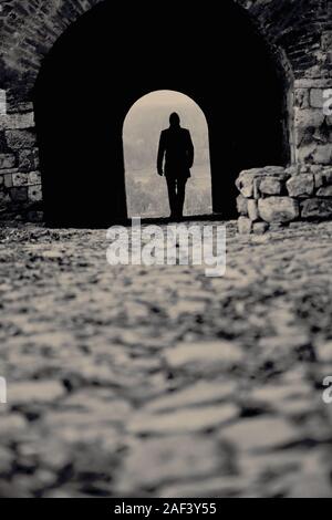 Silhouette d'un jeune homme marchant à travers un tunnel comme entrée d'une vieille forteresse Banque D'Images