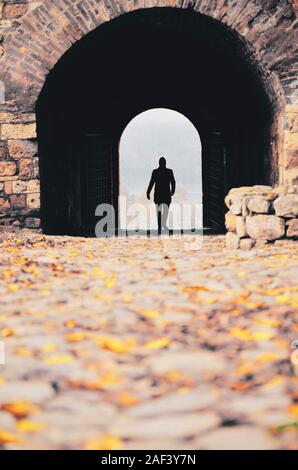 Silhouette d'un jeune homme marchant à travers un tunnel comme entrée d'une vieille forteresse Banque D'Images