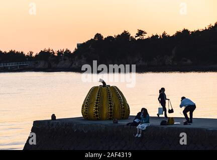 Les touristes prenant des photos avec Yayoi Kusama's sculpture de citrouille jaune géant au coucher du soleil à Naoshima, au Japon. Banque D'Images