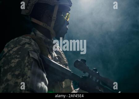 Vue de l'obscurité du soldat américain en uniforme et casque de tir avec arme et à la recherche à côté. Vue latérale du casque à ranker ayant le travail de nuit. Concept de l'armée. Banque D'Images