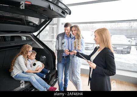 Voir du côté de votre femelle touches donnant de nouveau à des clients en voiture d'exposition automatique. Charmante famille achat de nouveau à l'aise dans l'automobile auto salon. Concept de vente au détail de voiture. Banque D'Images