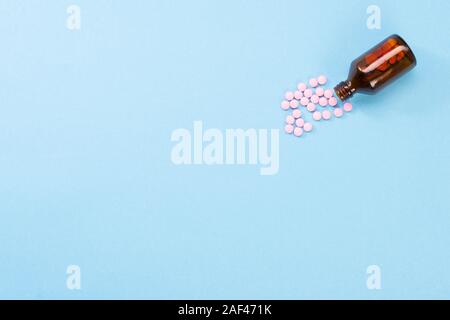 Pilules roses et le flacon en verre sur un fond bleu. Concept de soins de santé et des pilules. Flatlay Vue de dessus. Copyspace pour le texte Banque D'Images