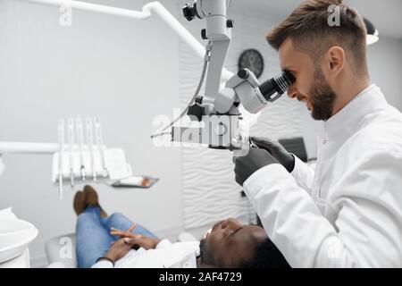 Vue latérale du dentiste professionnel en uniforme blanc et noir des gants de garder l'équipement et de l'examen des dents du patient. Jeune médecin soigner les dents. Concept de traitement et de la santé.