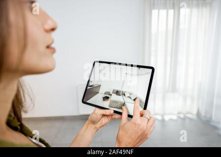 Jeune femme en plaçant de nouveaux meubles sur une tablette numérique dans le vide intérieur, à quoi il ressemble avant d'acheter. Concept de la réalité augmentée dans la conception et commerce de détail Banque D'Images