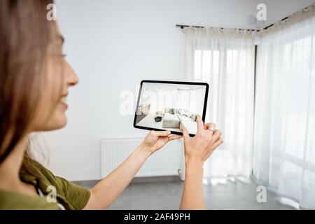 Jeune femme en plaçant de nouveaux meubles sur une tablette numérique dans le vide intérieur, à quoi il ressemble avant d'acheter. Concept de la réalité augmentée dans la conception et commerce de détail Banque D'Images