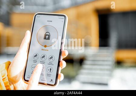 Holding phone avec alarme lancé app sur le fond de la chambre à l'extérieur. Concept de contrôle et la gestion de la sécurité à la maison à partir d'un terminal mobile Banque D'Images