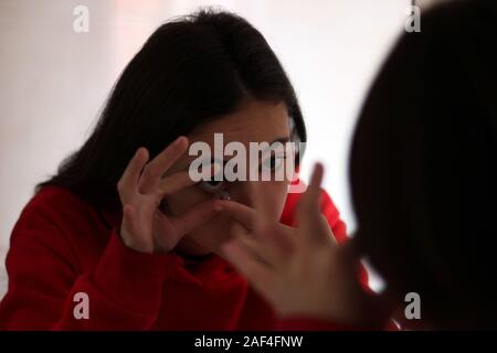 Jeune et jolie fille prise de ses verres de contact dans sa salle de bains privative. Concept de la santé oculaire. Banque D'Images