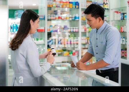 Asian young female pharmacist avec un beau sourire amical et expliquer à son client la médecine dans la pharmacie pharmacie. La médecine, pha Banque D'Images