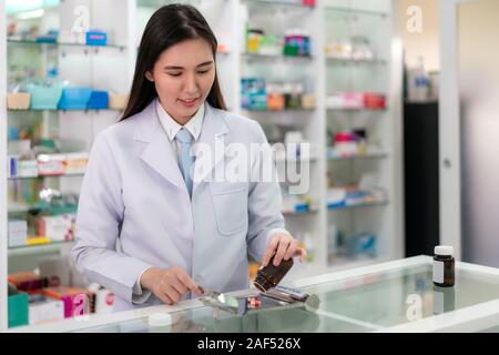 Jeune femme asiatique pour le pharmacien et de compter les capsules sur le bac acier inoxydable, elle prépare la pack à patient dans la pharmacie en ligne. La médecine, pha Banque D'Images