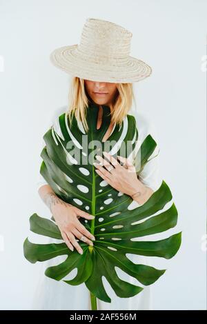 Jeune femme élégante avec chapeau à la feuille de palmier sur fond blanc Banque D'Images