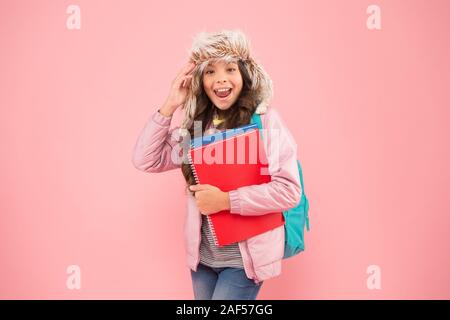 Sentir l'esprit des vacances d'hiver. vacances. et de vêtements chauds pour enfants fond rose. élève la vie quotidienne. lycéenne sac à dos et livres vont à la maison. pas de plus d'examens. petite fille heureux chapeau earflap. retour à l'école. Banque D'Images