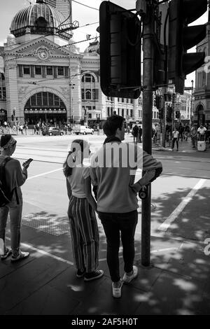 Jeune couple d'attendre pour traverser la rue Swanston Melbourne, avec la gare de Flinders Street en arrière-plan. Banque D'Images