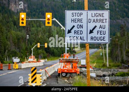 Selective focus sur une route blanche signe sur poteau en bois, route de la zone de travail avec des machines à l'arrière-plan, s'arrêter ici sur le signal rouge, avec la flèche Banque D'Images