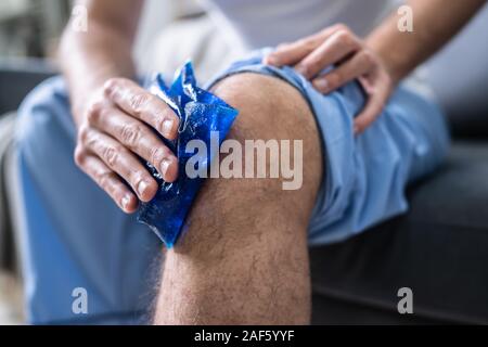 Close-up d'une personne assise à l'application de glace et de gel sur un genou blessé Banque D'Images