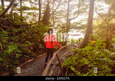 Fille aventureuse marche dans une forêt avec une vue magnifique sur la côte de l'océan lors d'un lever de soleil coloré dynamique. Sentier sauvage Pacifc, Ucluelet, Vancouve Banque D'Images