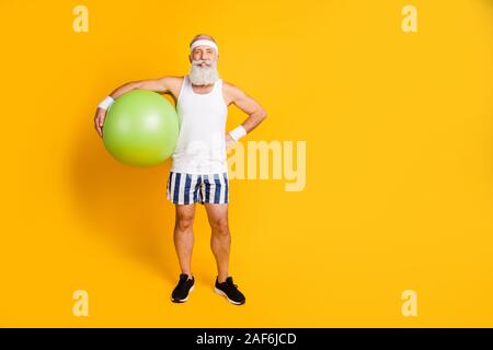 Photo de tout le corps de hauts guy holding big green fit ball prêt commencer la formation de manière active d'usure de la vie haut-réservoir sport short sweatband sneakers Banque D'Images