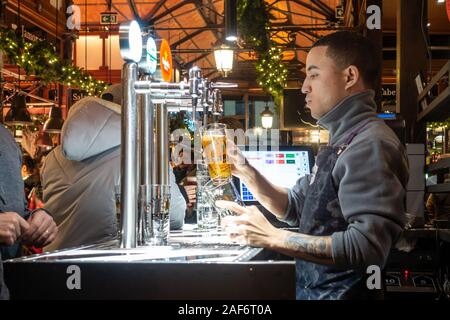 Un barman verse une bière pour un client de Mercado San Miguel, un marché couvert à Madrid, en Espagne, qu'on voit ici dans la soirée près de Noël. Banque D'Images