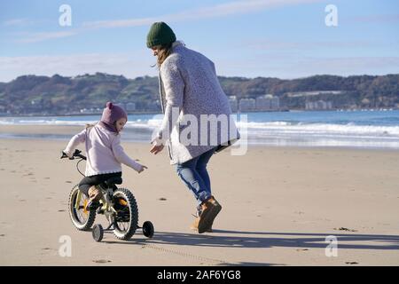 Mère d'exécution à côté de jeune fille vélo on beach Banque D'Images